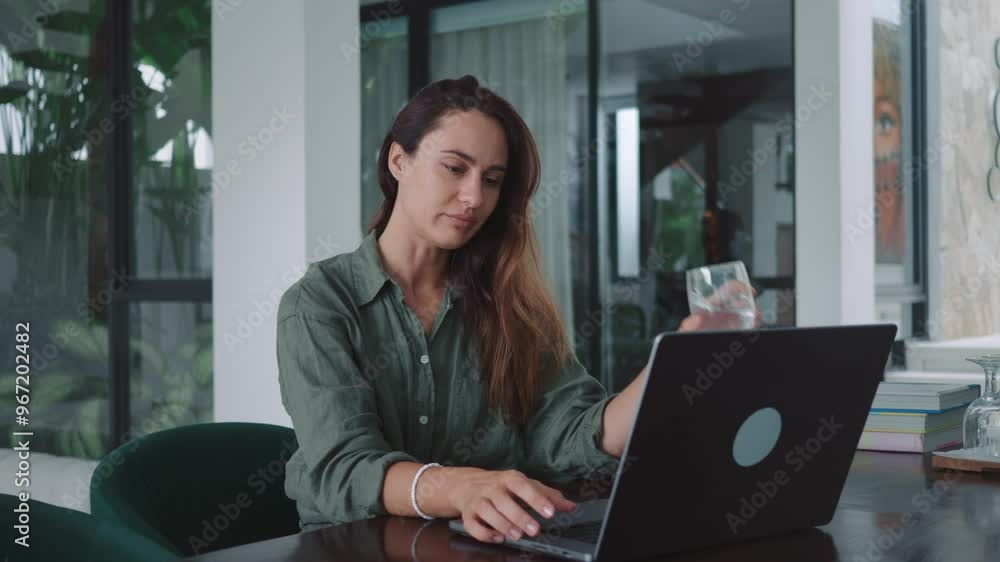 Caucasian lady sitting at desk focused on computer screen while sipping water remote work with modern technology. Modern young adult woman works at laptop pausing to drink from glass of water. Caucasian lady sitting at desk focused on computer screen while sipping water remote work with modern technology. Modern young adult woman works at laptop pausing to drink from glass of water.