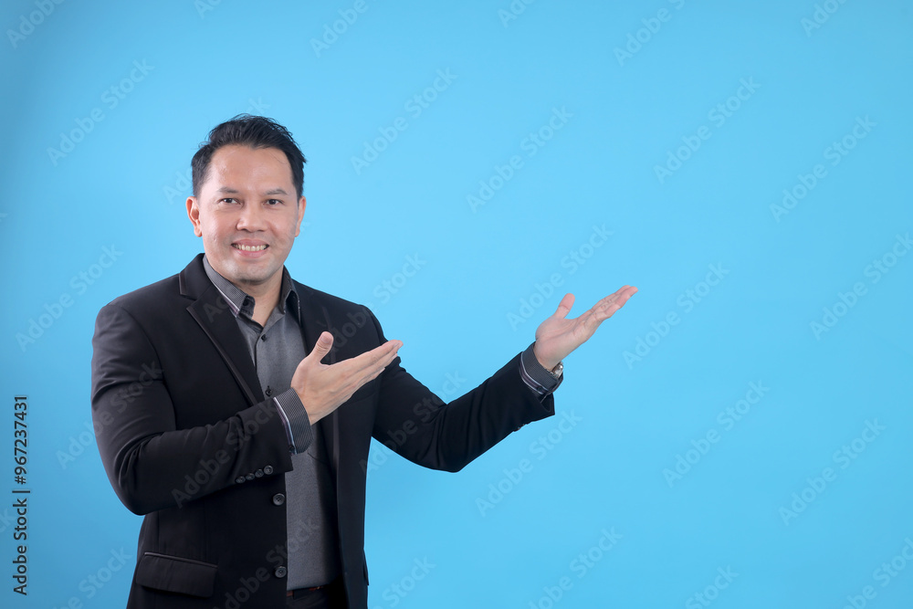 Happy Asian businessman showing and presenting something isolated on blue background Happy Asian businessman showing and presenting something isolated on blue background