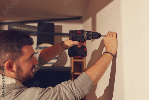 Fotografija Handyman with battery drill fixing kitchen cabinets and shelf.