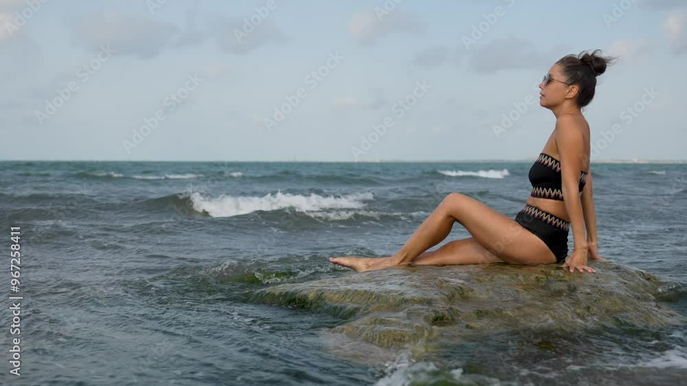 Young woman sitting on a rock enjoying the ocean waves. Beautiful woman relaxing on sea beach Young woman sitting on a rock enjoying the ocean waves. Beautiful woman relaxing on sea beach