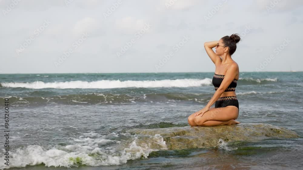 Young woman sitting on a rock enjoying the ocean waves. Beautiful woman relaxing on sea beach Young woman sitting on a rock enjoying the ocean waves. Beautiful woman relaxing on sea beach