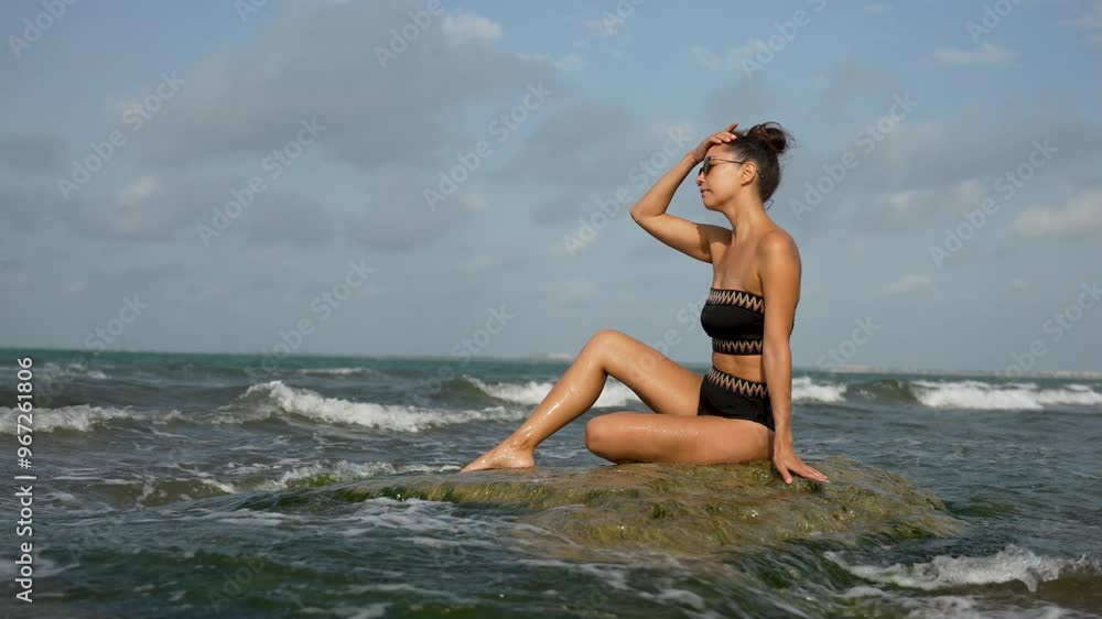 Young woman sitting on a rock enjoying the ocean waves. Beautiful woman relaxing on sea beach Young woman sitting on a rock enjoying the ocean waves. Beautiful woman relaxing on sea beach