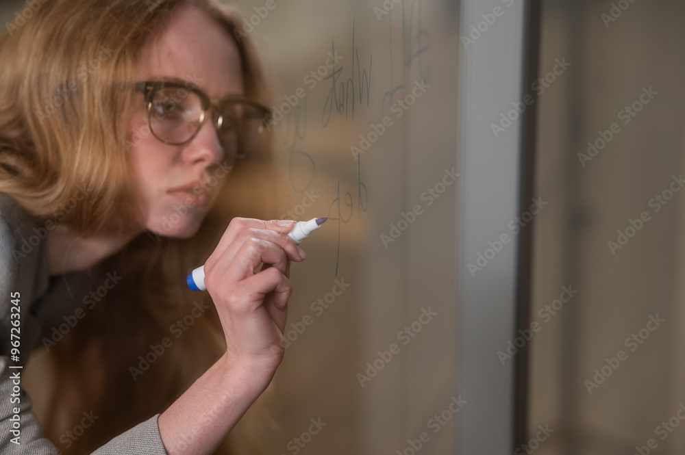 Caucasian woman with glasses writes text in English on a glass wall. Caucasian woman with glasses writes text in English on a glass wall.