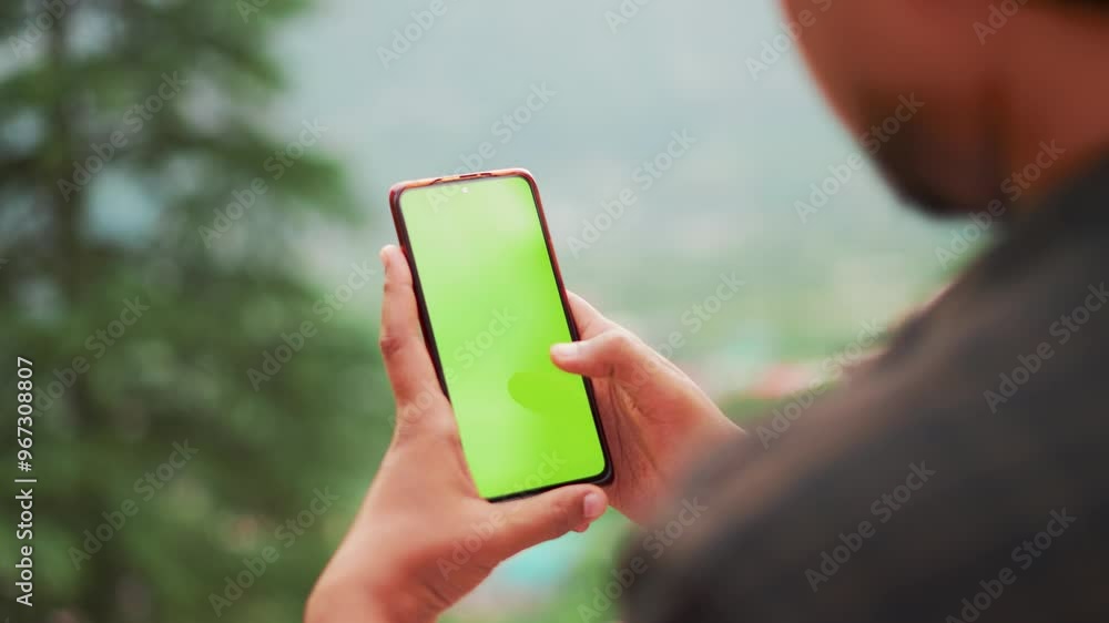 4K Closeup shot of Indian man using mobile phone with green screen while standing outdoors, Chroma Key display in young man hand. Man using Mobile phone vertically with isolated mockup template. 4K Closeup shot of Indian man using mobile phone with green screen while standing outdoors, Chroma Key display in young man hand. Man using Mobile phone vertically with isolated mockup template.