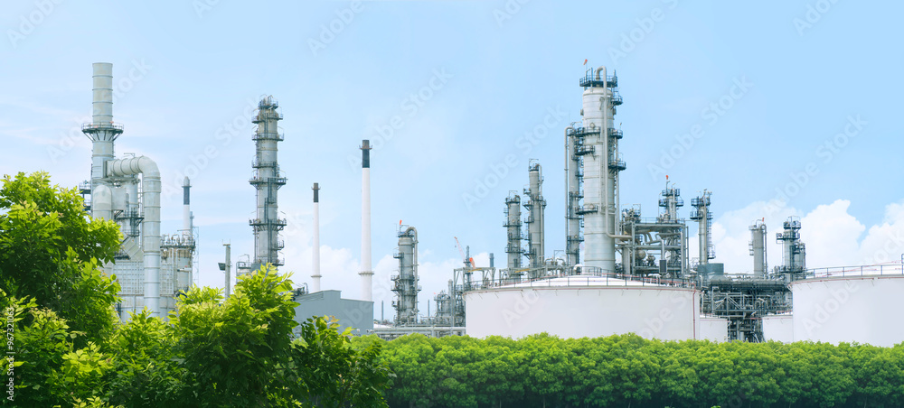 Obraz premium Oil refinery plant from industry zone with lush green trees and blue sky, large Oil and gas petrochemical industrial, Refinery factory oil storage tank and pipeline, Ecosystem and good environment.