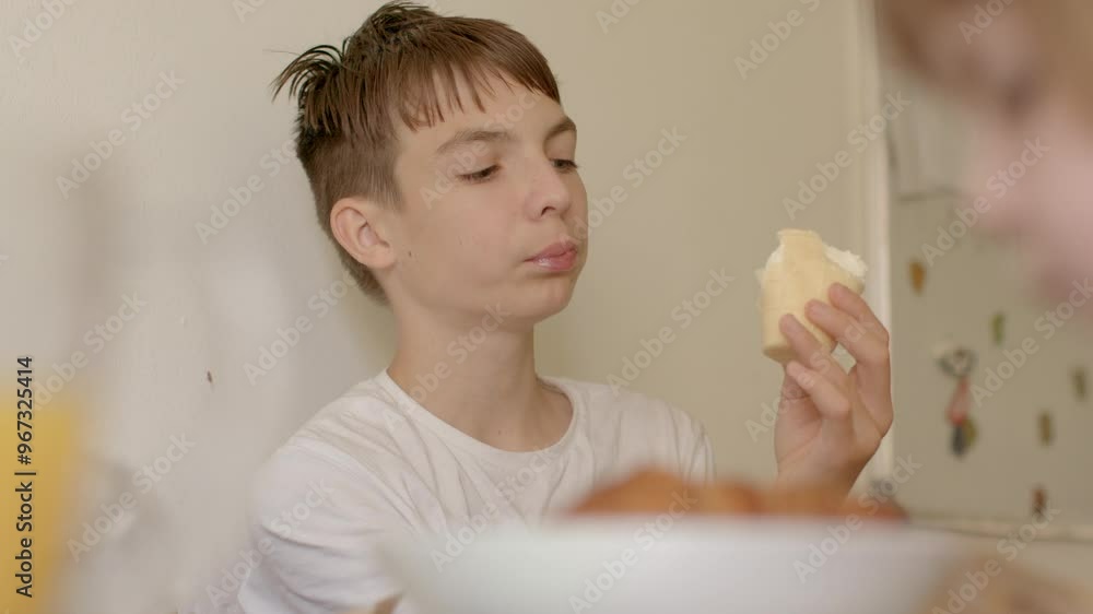 he eats food with his hands, looks at the piece, mindful eating young boy happily sits at the kitchen table, eagerly enjoying a tasty sandwich during a lovely breakfast