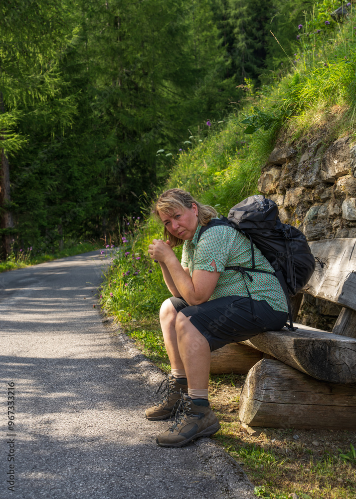 Woman with backpack is very tired on hike. She rests little and goes on her way. Sitting on bench on trail with alpine mountain peaks. Grossglockner. Hohe Tauern National Park, Austria. Hiking Woman with backpack is very tired on hike. She rests little and goes on her way. Sitting on bench on trail with alpine mountain peaks. Grossglockner. Hohe Tauern National Park, Austria. Hiking