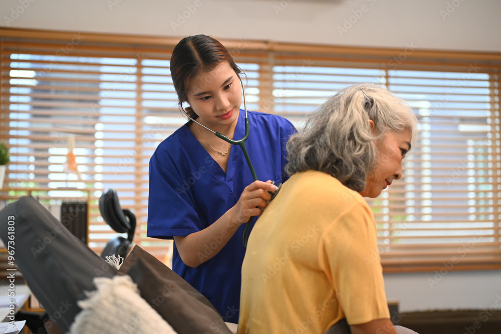 Healthcare professional in blue scrubs using a stethoscope to check breathing of an elderly female patient Healthcare professional in blue scrubs using a stethoscope to check breathing of an elderly female patient
