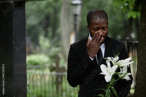 Obraz na plátne Medium shot of African American man in funeral black suit grieving at graveyard