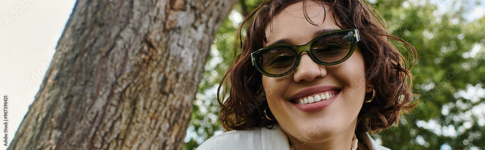 A young woman smiles brightly while relaxing in a vibrant green park during the warm summer days. A young woman smiles brightly while relaxing in a vibrant green park during the warm summer days.