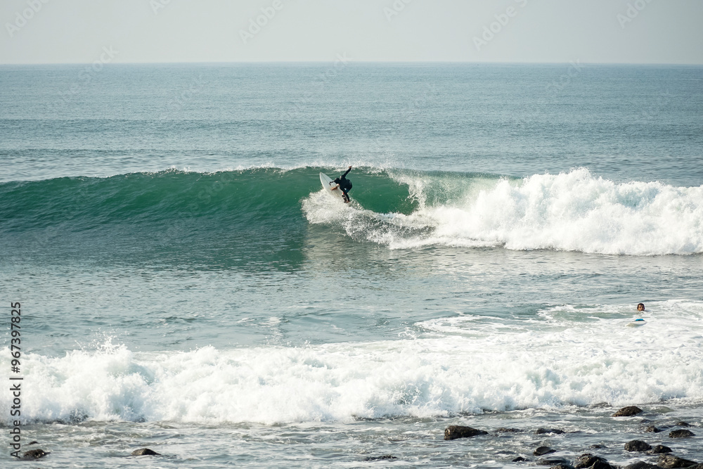 Surfer riding a wave along the rocky coast Surfer riding a wave along the rocky coast