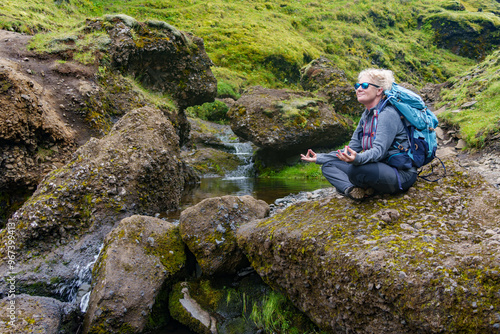 Woman meditating on rocks by a small stream in Icelandic landscape