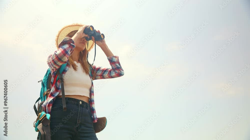 Female tourist visiting an island in summer stands with backpack and uses binoculars to enjoy the bird's-eye view white sandy beach and the beautiful scenery of the island with great enjoyment. Female tourist visiting an island in summer stands with backpack and uses binoculars to enjoy the bird's-eye view white sandy beach and the beautiful scenery of the island with great enjoyment.