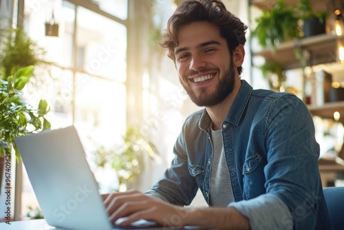 High-resolution brightly lit photorealistic candid photograph of a young marketer smiling while working on his laptop in a stylish office with natural light. The photograph is styled like a high-end