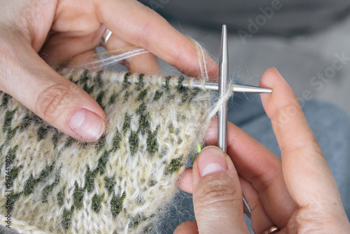 Obraz na płótnie Norwegian knitted pattern in woman hands. Girl holding knitting needles and beautiful knitting pattern. Woman with green and beige knitted pattern. Knitting hobby. Needlework background. w salonie