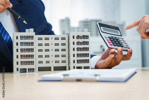  A businessman at a desk in a sales office sells a condo building to a customer. They agree to sign a contract, covering real estate investments in offices, apartments, and commercial properties.