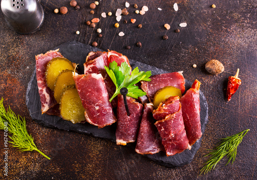 Dried Pastrami slices, beef meat with herbs on black board.