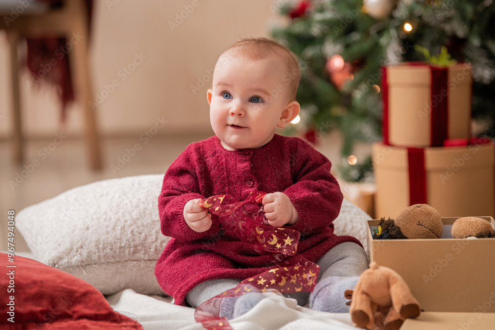 cheerful baby sits among gift boxes and toys next to a Christmas tree. cheerful baby sits among gift boxes and toys next to a Christmas tree.
