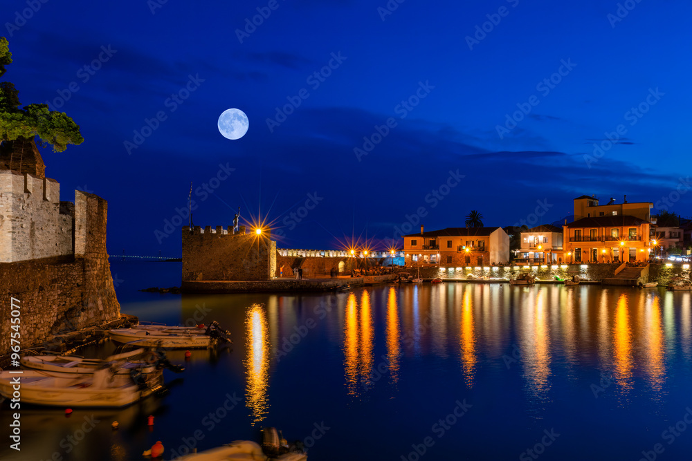 Lights reflecting water at the port of Nafpaktos in Greece against the full moon.