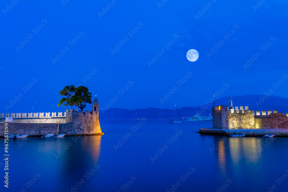 Blue hour in Nafpaktos port in Greece against the full moon.