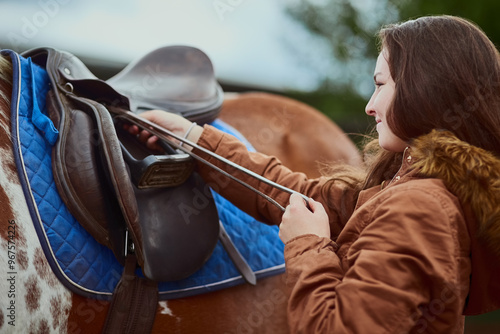 Horse, girl and adjust saddle outdoor for race, sport and training at countryside or farm. Animal, equestrian and prepare strap or gear for riding with pet for care with teenager at horseback school