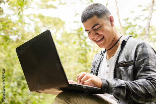 A young Latino biologist is happily working outdoors with a laptop, an independent person working among trees