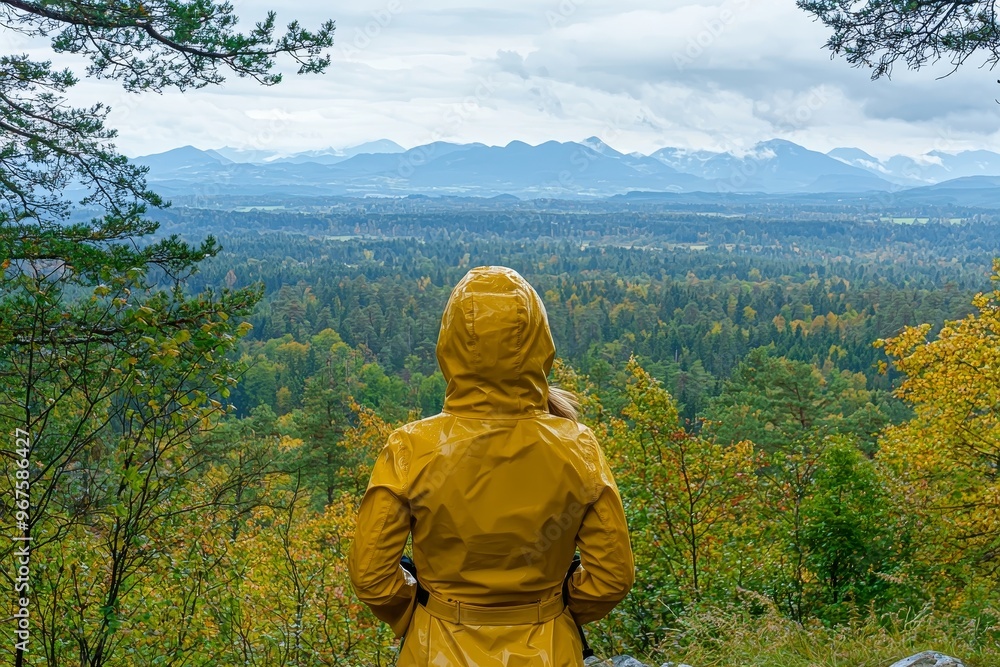 The scenic beauty of the valley and mountains is admired by a woman wearing a yellow raincoat on a hill. The scenic beauty of the valley and mountains is admired by a woman wearing a yellow raincoat on a hill.