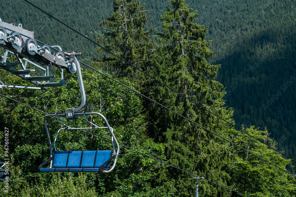 A chairlift ascends through lush green trees in the mountains during a clear summer day