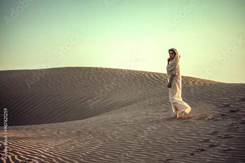 Woman in flowing dress atop desert dune. Golden light, rippled sand. Evokes adventure, solitude, and timeless beauty. Perfect for travel and lifestyle themes.