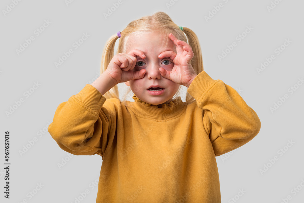 Portrait of a cute little girl looking through her fingers like binoculars on a gray background Portrait of a cute little girl looking through her fingers like binoculars on a gray background