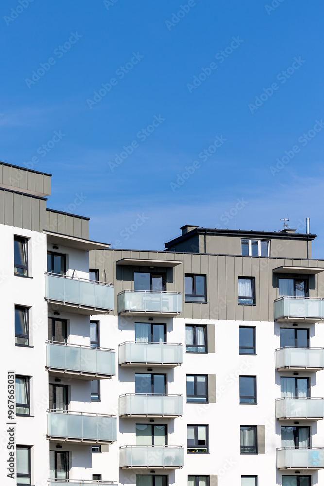 White and beige facade of a newly built apartment block. Clear blue sky above the building. Photo taken on a sunny day