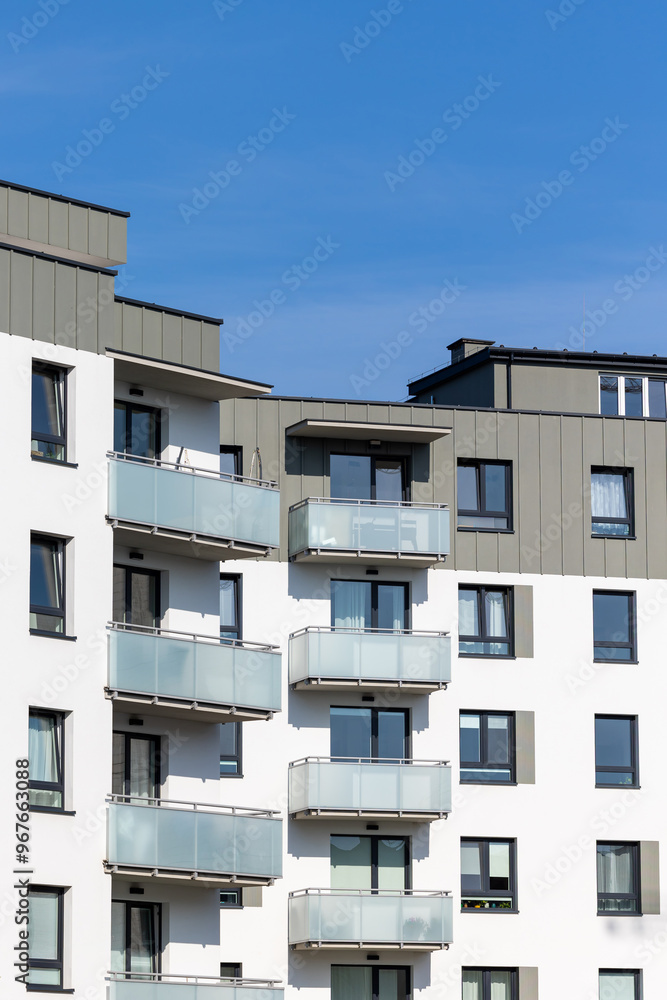 White and beige facade of a newly built apartment block. Clear blue sky above the building. Photo taken on a sunny day