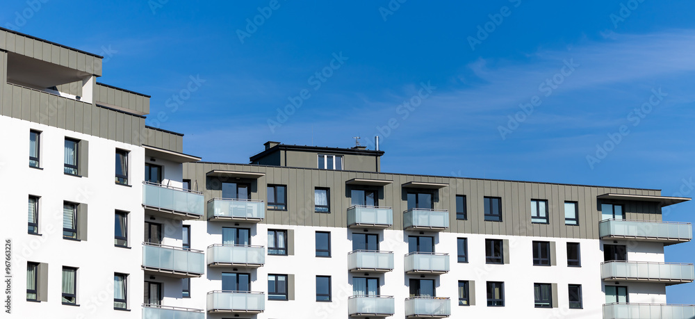 White and beige facade of a newly built apartment block. Clear blue sky above the building. Photo taken on a sunny day