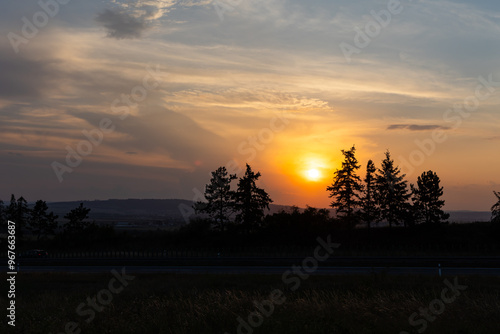 Obraz na płótnie Orange sunset sun getting down amongs the trees over the road in the shade. Dramatic orange sky during the susnset. w salonie