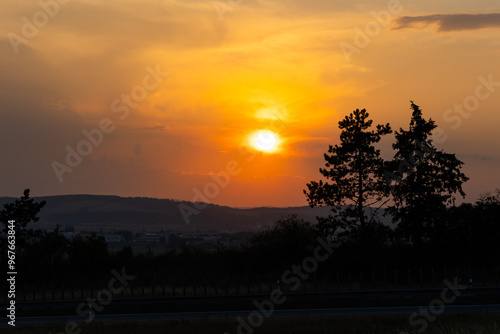 Obraz na płótnie Orange sunset sun getting down amongs the trees over the road in the shade. Dramatic orange sky during the susnset. w salonie