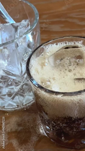 spill cola on the table tream of cola pours into a glass, creates a splash and a drop flows down the edge, a sparkling shadow on a wooden brown table, side view photo