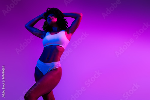 Portrait of gorgeous model girl perfect body shape hands touch head empty space isolated on vibrant purple neon background photo