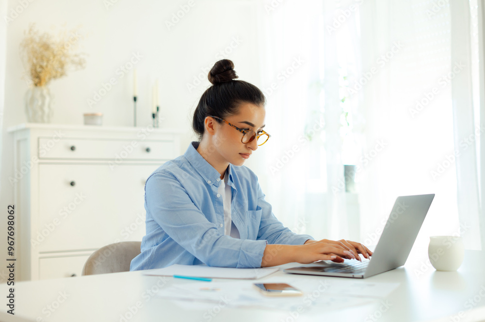 Focused serious business woman of arabian or indian ethnicity in blue shirt, digital manager, company ceo, sits at a workplace while working on a laptop, concentrated looks at a screen, searching info Focused serious business woman of arabian or indian ethnicity in blue shirt, digital manager, company ceo, sits at a workplace while working on a laptop, concentrated looks at a screen, searching info