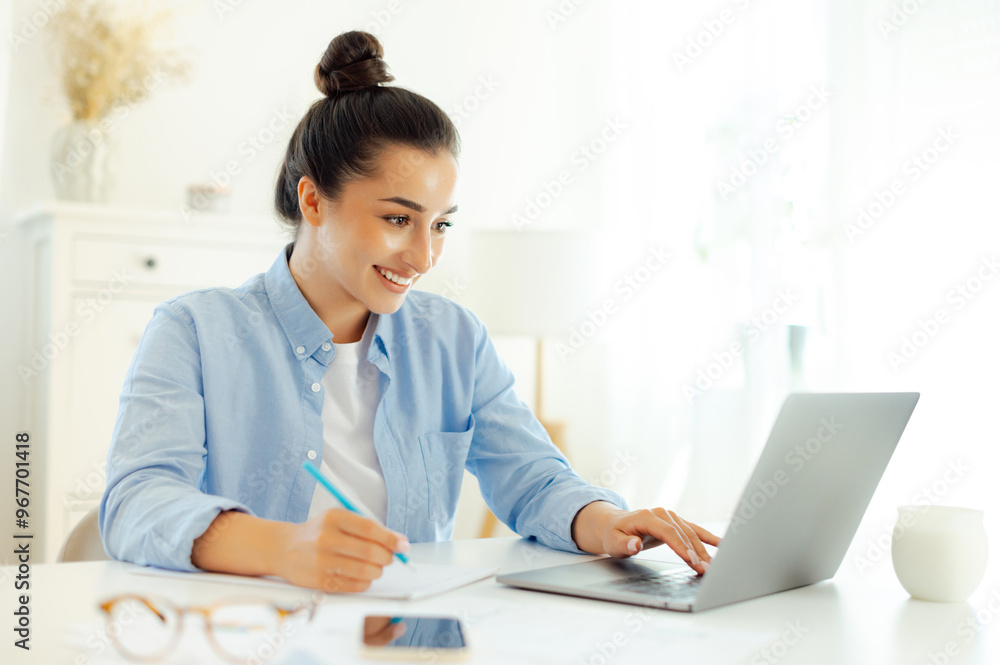 Happy successful arabian or indian business woman in a blue shirt, project manager, company ceo, working on a laptop, develop strategy and business plan, takes notes, searching information, smiles Happy successful arabian or indian business woman in a blue shirt, project manager, company ceo, working on a laptop, develop strategy and business plan, takes notes, searching information, smiles