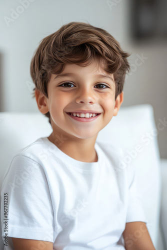 A smiling child boy sitting in a white medical office on a couch for an examination.