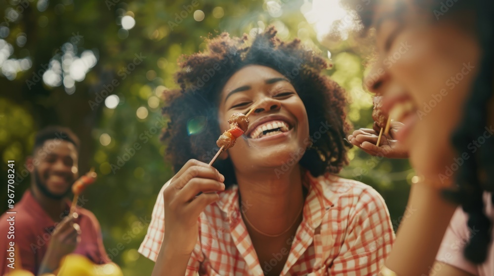 Fototapeta Friends share a joyful moment at a sunny picnic, savoring skewered food and enjoying each other's company in a lush garden.