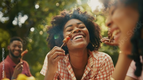 Friends share a joyful moment at a sunny picnic, savoring skewered food and enjoying each other's company in a lush garden.