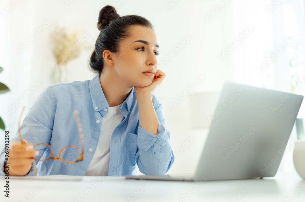 Concerned business woman of arabian or indian ethnicity in a blue shirt, company manager or digital seo, sits at a workplace with a laptop, worried about work deadlines, feels stressed and overworked Concerned business woman of arabian or indian ethnicity in a blue shirt, company manager or digital seo, sits at a workplace with a laptop, worried about work deadlines, feels stressed and overworked