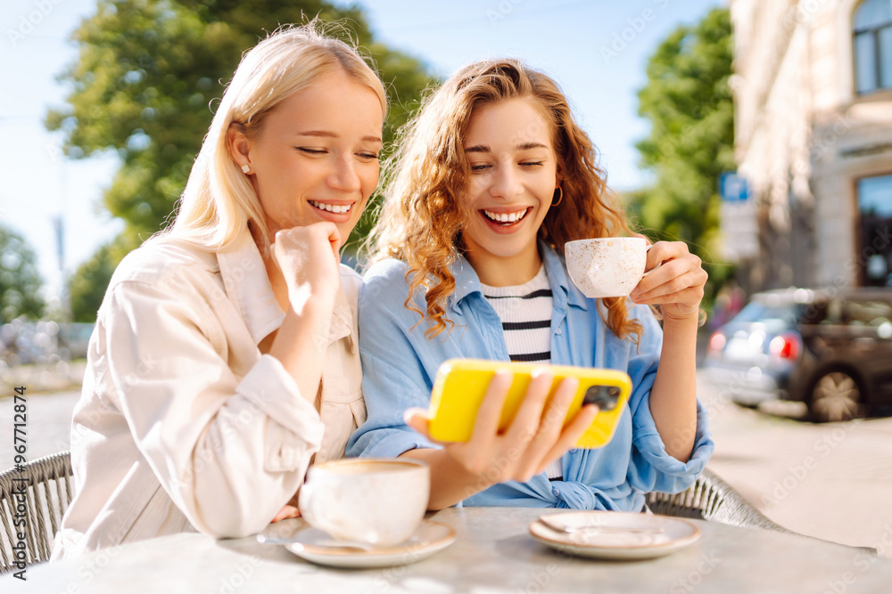 Friends share a joyful moment at an outdoor café, sipping coffee and taking selfies in the warm afternoon light, creating lasting memories together. Fashion, beauty, blogging, tourism.