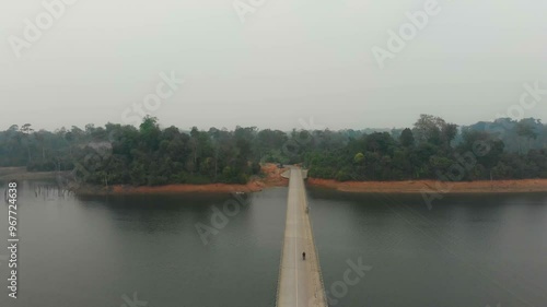 Aerial view of a tranquil river with a bridge and a motorbike surrounded by serene forest, Nam Theun, Khammouane, Laos. photo