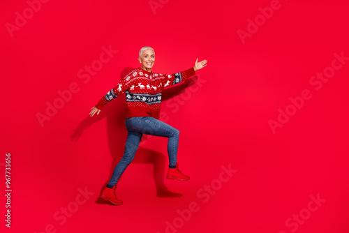 Full body photo of attractive senior woman walk excited empty space dressed theme party sweater isolated on red color background