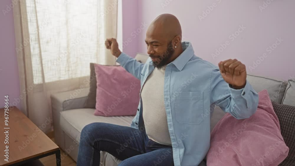 Handsome young man stretching in a cozy living room with soft pillows, enjoying a peaceful moment indoors.