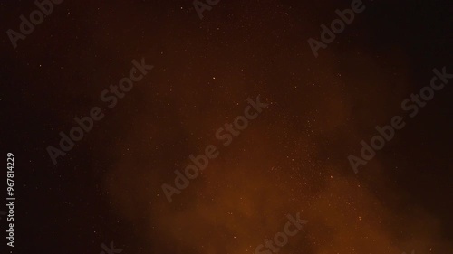 Fire sparks and ember particles from a bonfire light up the dark night sky as they rise up with smoke