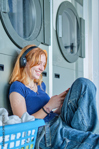 Smiling redhead girl listening to music in a public laundry waiting for her clothes to be washed
