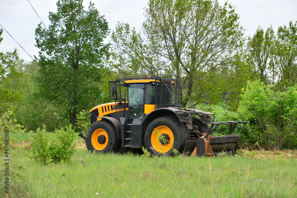 a yellow tractor on the green field with some trees in the background a yellow tractor on the green field with some trees in the background